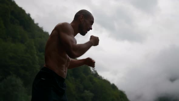 a Male Silhouette with a Bare Torso Against the Background of a Green Mountain and a Bright Sky