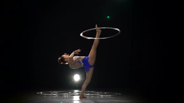 Girl Gymnast Turns the Metal Hoop on the Arm Then on the Leg. Black Background. Slow Motion