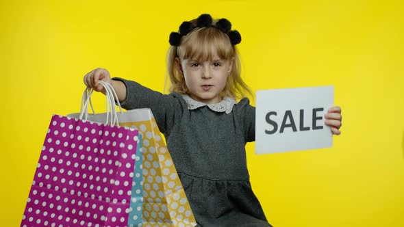 Cute Joyful Kid Girl in Shirt Showing Sale Word Advertisement Inscription Banner and Shopping Bags