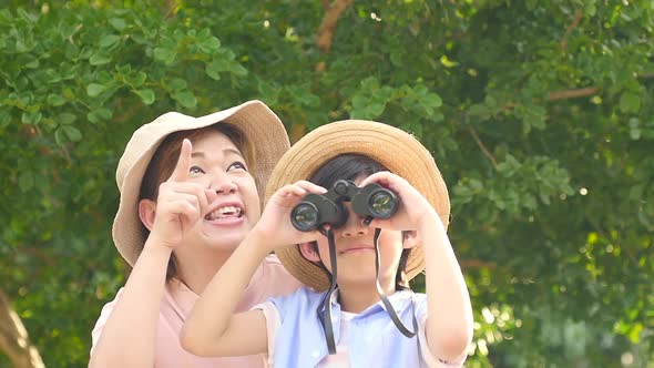 Asian Mother And Her Son Using Binocular And Pointing On Summer Day