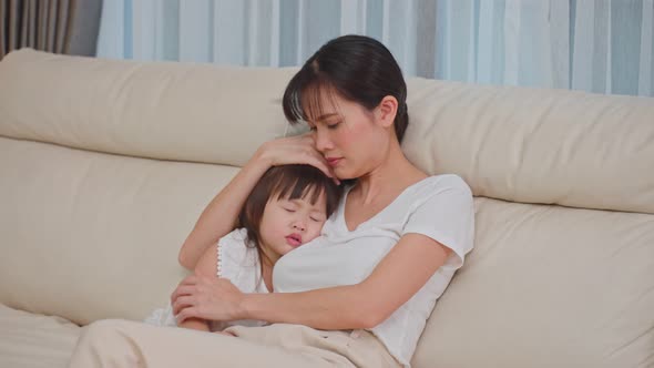 Asian mother hugging sleeping baby cute girl in her arms with gently on sofa at home concept.