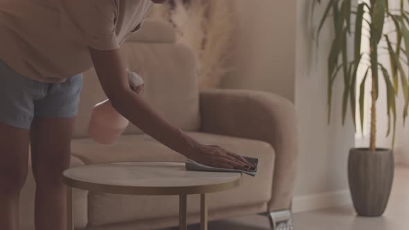 Young Woman Wiping Coffee Table in Sunlit Apartment