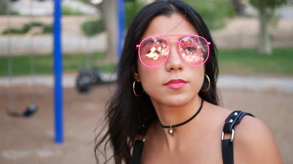 An attractive hispanic woman hipster with retro pink sunglasses in a colorful park playground swing