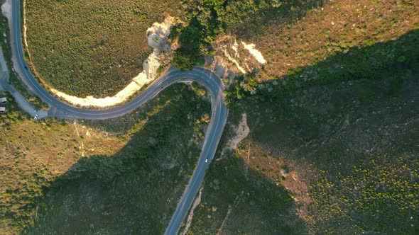 car driving on Chapmans Peak Road on coast of Cape Town at sunset, top down aerial