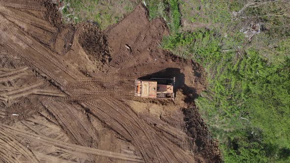 Top aerial view of bulldozer flattening surface on further construction site