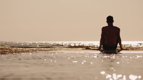 Back View of Alone Young Man Sitting on a Small Sand Island