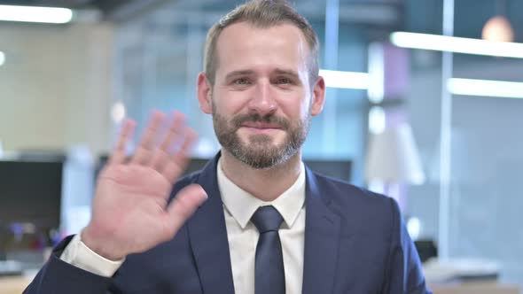 Portrait of Young Businessman Waving at Camera in Office