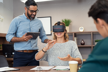 to woman wearing virtual glasses at office. Happy smiling client trying virtual reality in office with business team. Cheerful woman making hand gestures while enjoying virtual reality with her multiethnic boss.