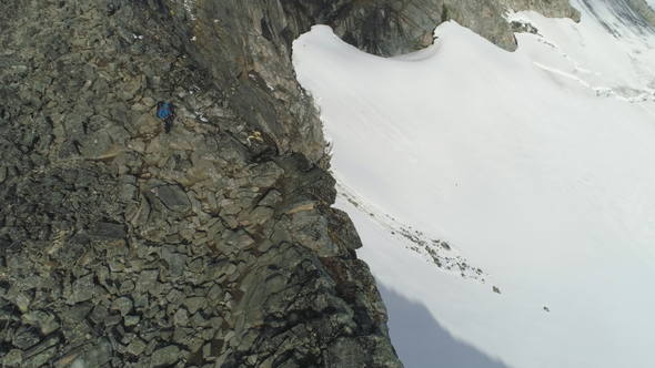 Hiker Man Is Hiking and Descending Near Cliff in Snowy Mountains of Norway. Aerial View