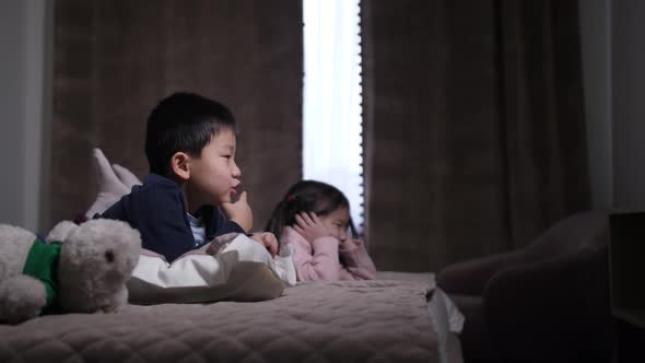 Cute Chinese Siblings Watching TV Lying on Bed