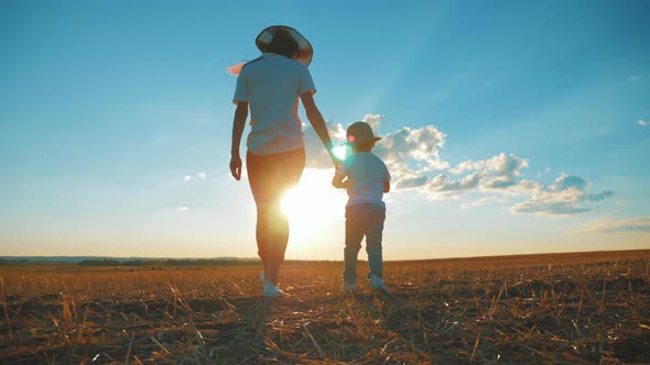 Mother and Little Son Playing on Meadow. Boy Raising Up Hands at Wonderful Sunset