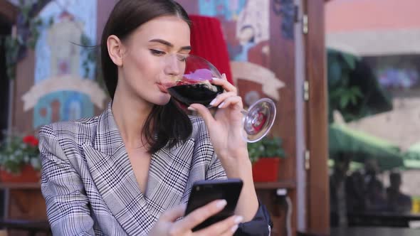 Smiling Woman Drinking Wine And Using Phone At Restaurant