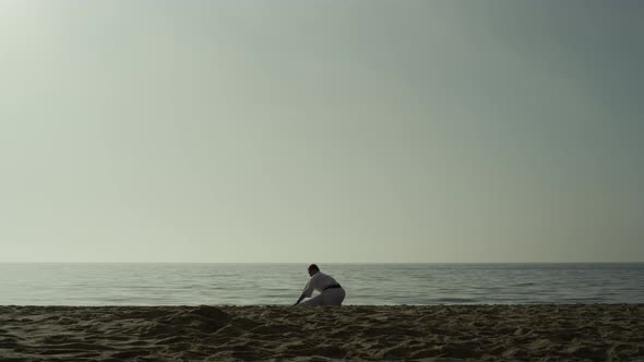 Sporty Man Doing Warmup Squatting on Sand