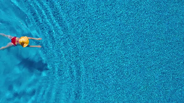 View From the Top As a Woman in a Red Swimsuit and a Big Yellow Hat Swims in the Pool