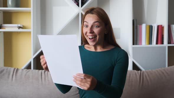 Happy Young American Woman Reading Paper Letter, Amazed By Good News, Sitting on Sofa at Home
