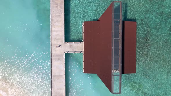 Woman standing on pier boat house of Gili Meno during beautiful summer day.Ascending aerial top down