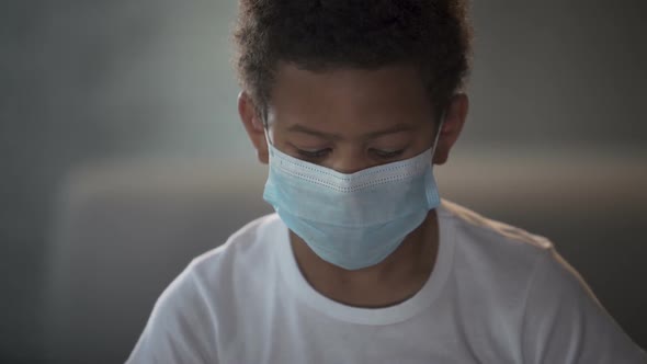 African American Child in Medical Mask Looking Into Camera With Sad Eyes