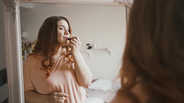 Young Plus Size Lady Applying Lipstick Making Everyday Make Up Looking at Mirror at Home and