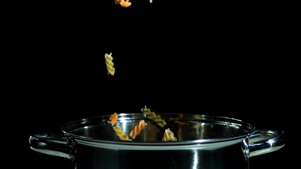 Fusilli falling in pot on black background