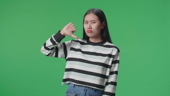 Asian Woman Showing Thumbs Down Gesture While Standing In Front Of Green Screen Background