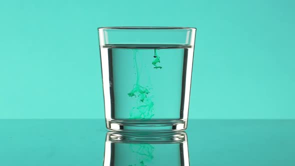Swirls of Green Ink in Clear Water in Glass Standing on Turquoise Background in Slowmotion
