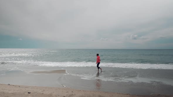 Slim female is walking along sea water waves on sandy beach