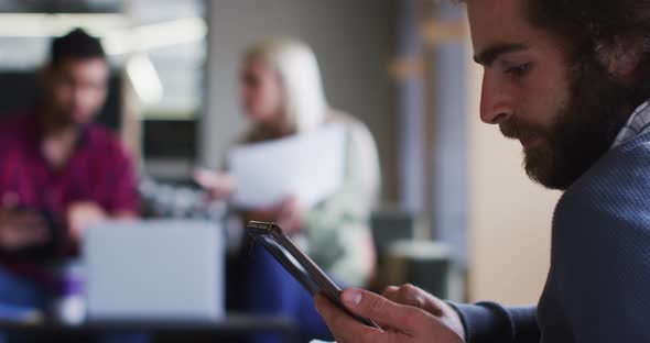 Diverse business people sitting using digital tablet and goign through paperwork in modern office