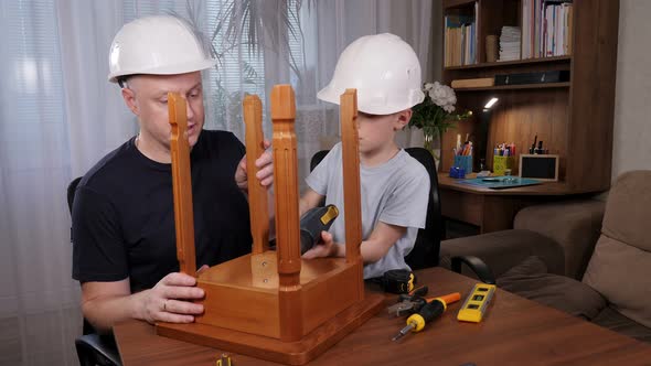 A Little Boy with His Father in White Helmets Fixing a Wooden Chair Together