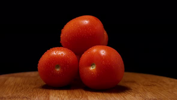 Ripe red juicy tomatoes with drops of condensation on a wooden background. The camera flies around
