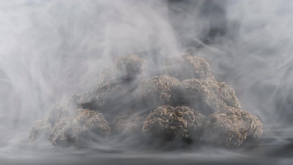 Close-up shot of cloud of smoke with cannabis marijuana buds on dark set.