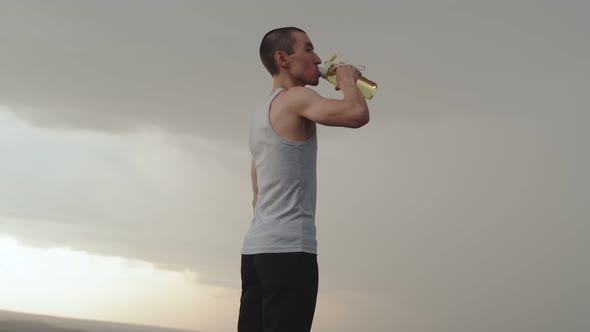 Asian Man Drinks Water From Sports Bottle After Jogging Outdoors Side View