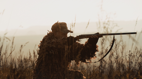 Hunter in hunting equipment lies in wait in the field