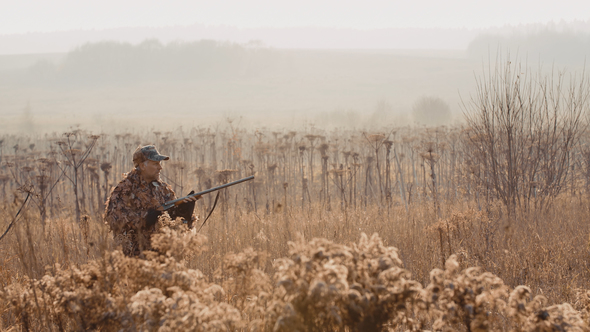 Hunter With a Rifle in His Hand Sneaks Through the Bush in the Field