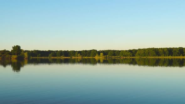 Panorama of a Large Lake with Quiet Water, Forest on the Opposite Bank Under a Blue Sky in the