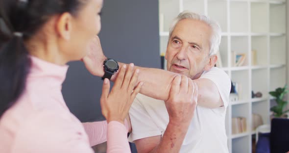 Video of happy biracial female physiotherapist exercising with caucasian senior man