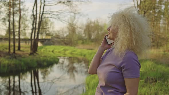 Woman Answering a Phone Call While Walking in the Park