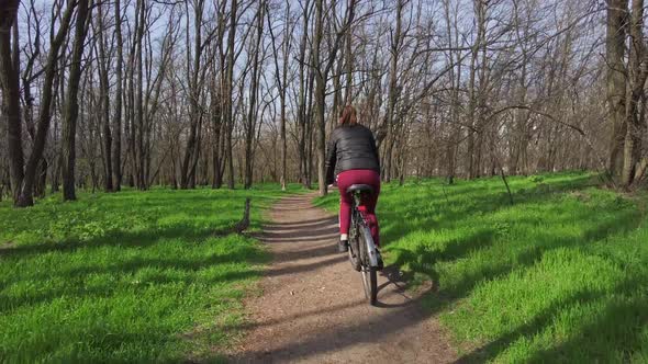 Young Woman on a Bicycle Rides Along a Path in the Forest in a Sunny Spring Day