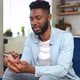 Cheerful Young Black Guy Sending Message on Mobile Phone While Sitting at the Sofa - VideoHive Item for Sale