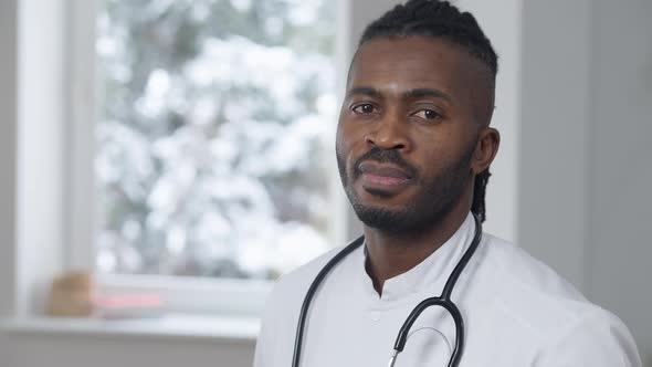 Positive Male African American Doctor in Uniform Turning Looking at Camera Standing Indoors