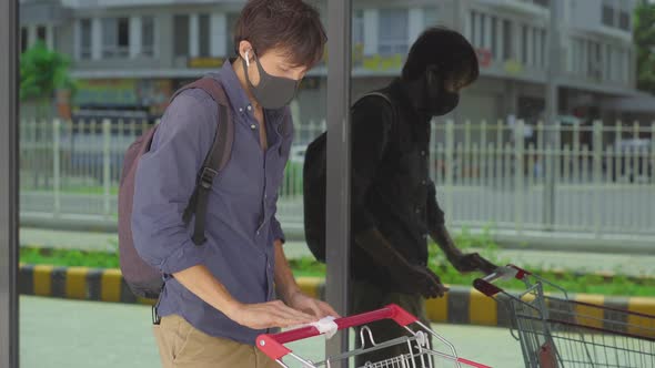 Young Man Disinfecting a Handle of a Supermarket Trolley in Order To Protect Himself From Contact