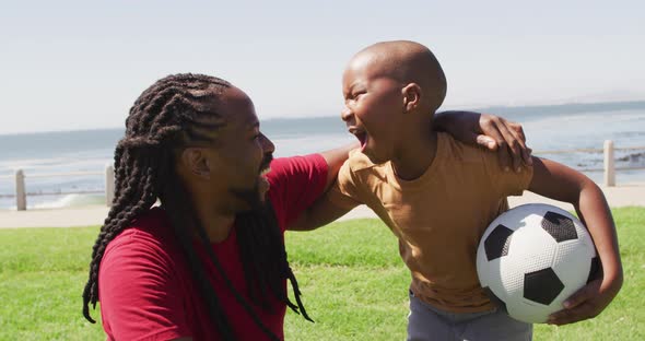 Video of happy african american father and son having fun with ball outdoors