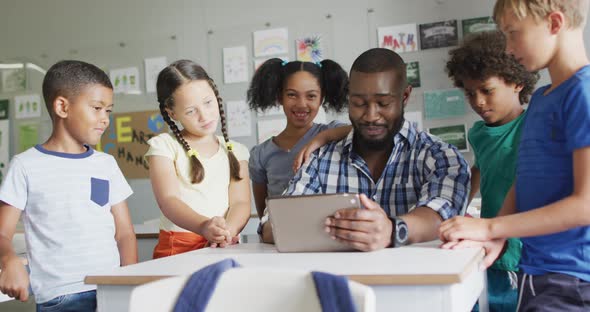 Video of happy african american male teacher and class of diverse pupils working on tablet