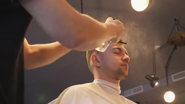 Close Up of Young Hairstylist Spraying Water on Male Hair From Sprayer After Cutting in Salon