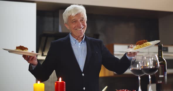 Portrait of Smiling Senior Man in Suit Holding Plates with Spaghetti Bolognese and Smiling at Camera