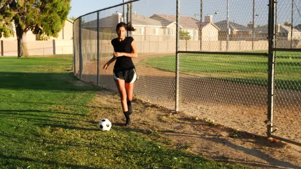 A female soccer player running with a football dribbling up the grass field during a team sport prac