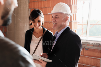 Man working as realtor in construction site with customers. Real estate broker showing home to husband and wife.