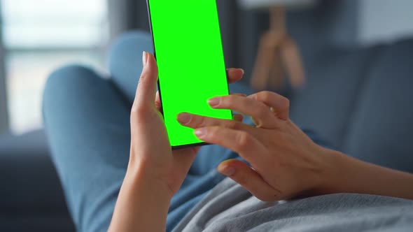 Woman at Home Lying on a Sofa and Using Smartphone with Green Mock-up Screen in Vertical Mode