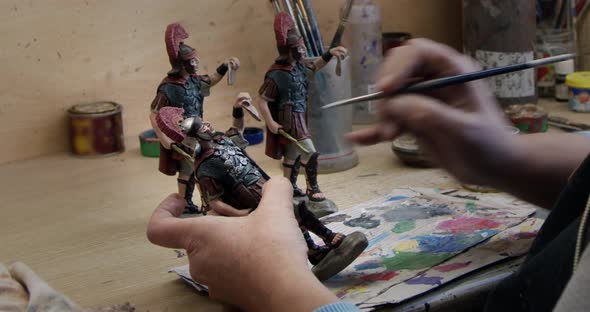 Painter painting clay figurines of soldiers at table