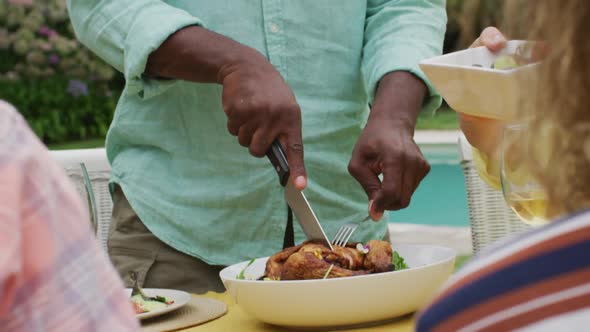 Happy african american senior man cutting meat for lunch with friends in garden