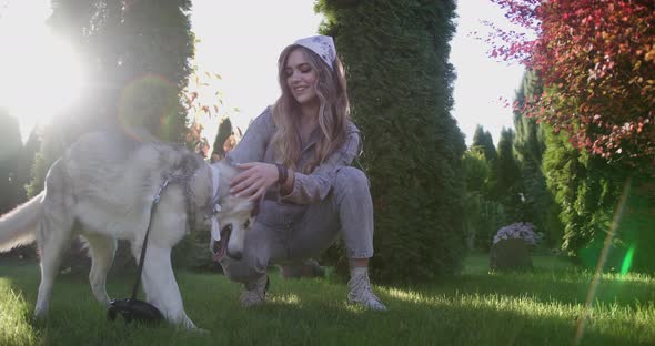 An Attractive Young Blonde Woman Play With Purebred Siberian Husky Dog In Park. Bright Sunny Day